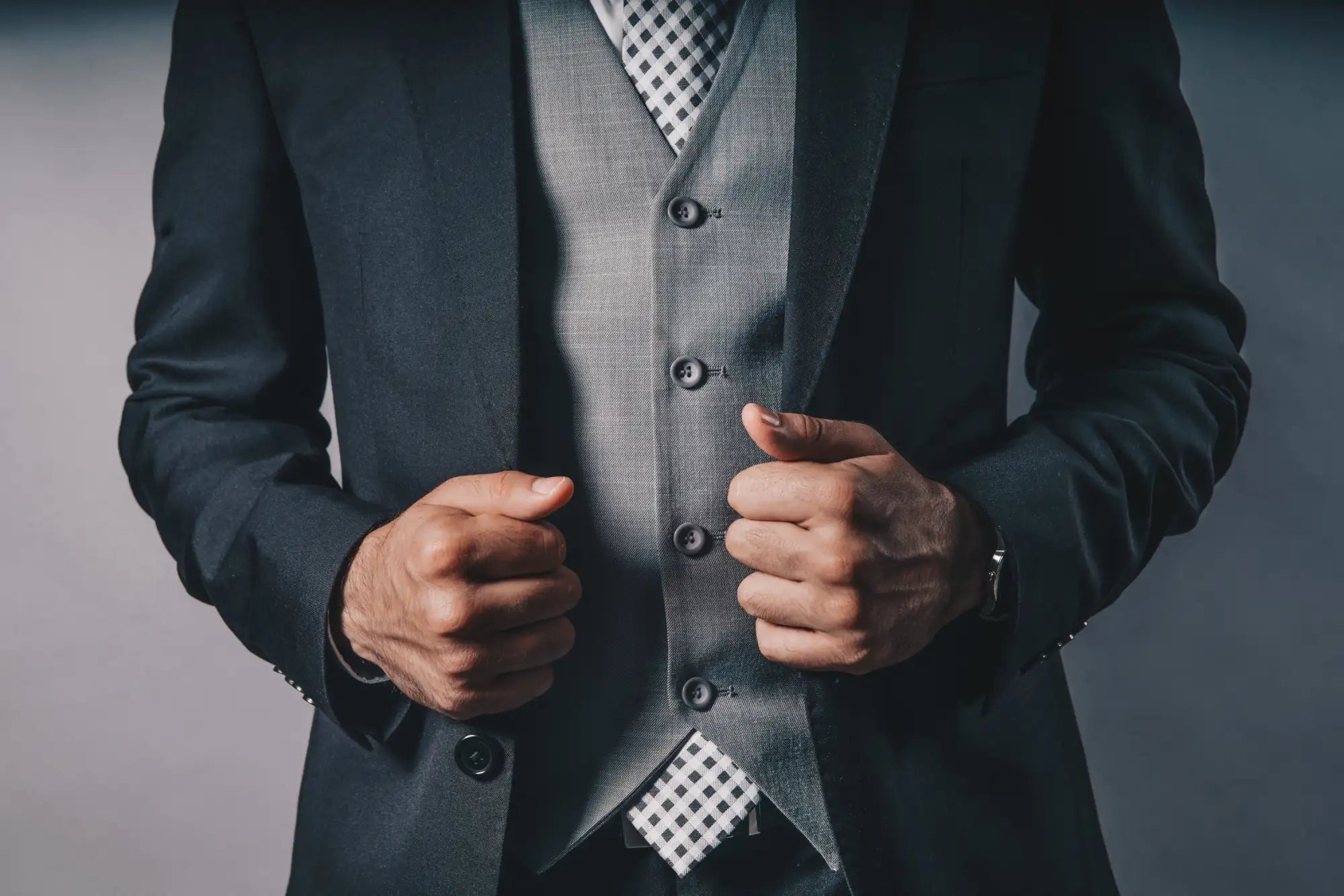 Dark navy suit jacket with a gray textured vest and black buttons, paired with a white-and-black checkered tie.